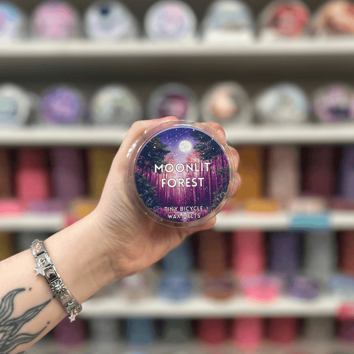 Moonlit Forest wax melt pot held in hand with colourful wax melt display in the background