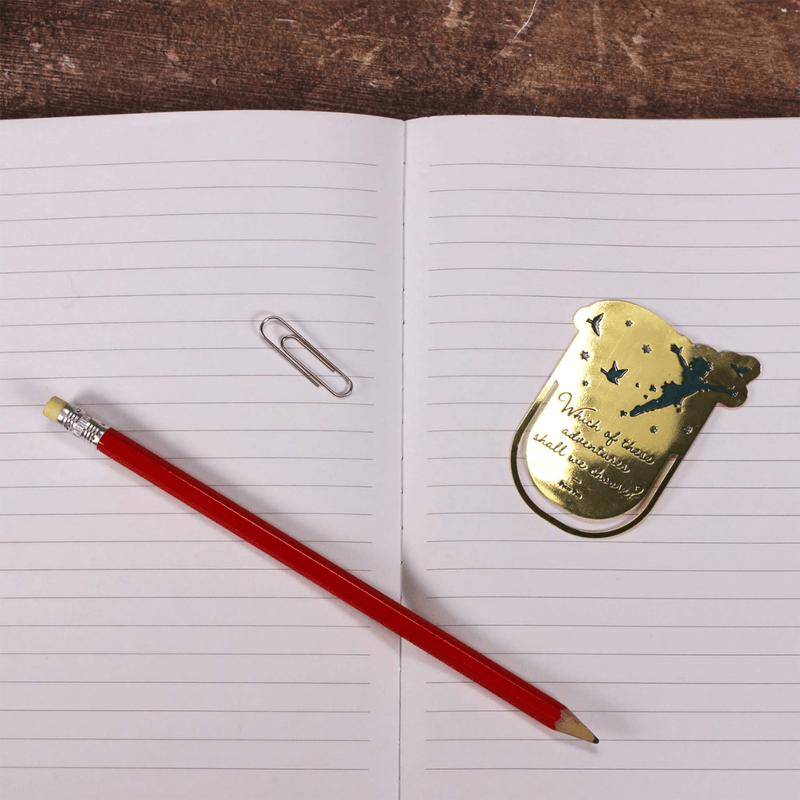 Gold Neverland metal bookmark with pencil and paperclip on an open notebook