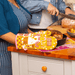 Funny mustard oven mitt on kitchen counter beside roasting dish and bread, lifestyle photo.
