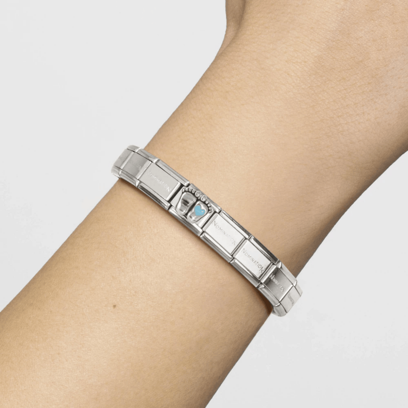 Nomination Classic stainless steel bracelet worn on the wrist featuring a silver baby footprints charm with blue heart detail.