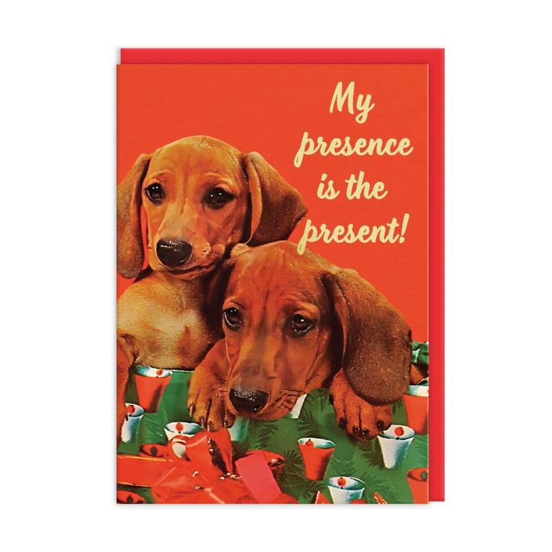 Red Christmas card with two dachshunds among presents; cream script reads My presence is the present; A6, gold foil, blank inside, brown kraft envelope by Ohh Deer