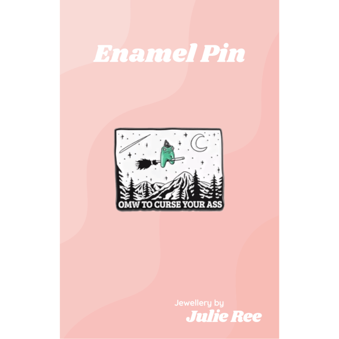 Black and white enamel pin with a tiny witch frog flying on a broom and the text OMW to curse your ass