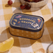 Paddywax Bistro Bordeaux Grape tin candle on a checked tablecloth with grapes and lemon
