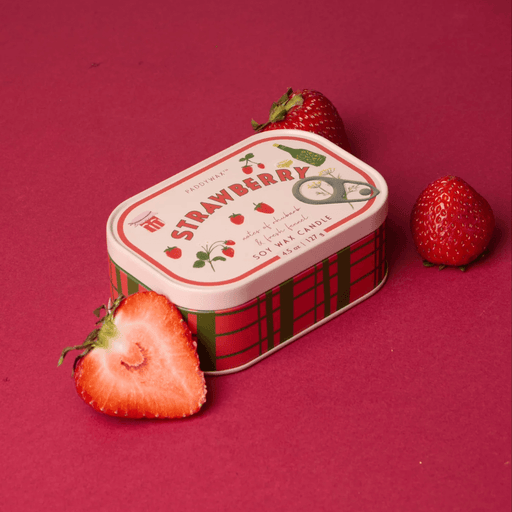 Paddywax Bistro Strawberry tin candle displayed with fresh strawberries on a red background