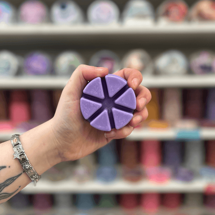 Purple Pandora's Box wax melt segments held in hand with colourful wax melt display in the background