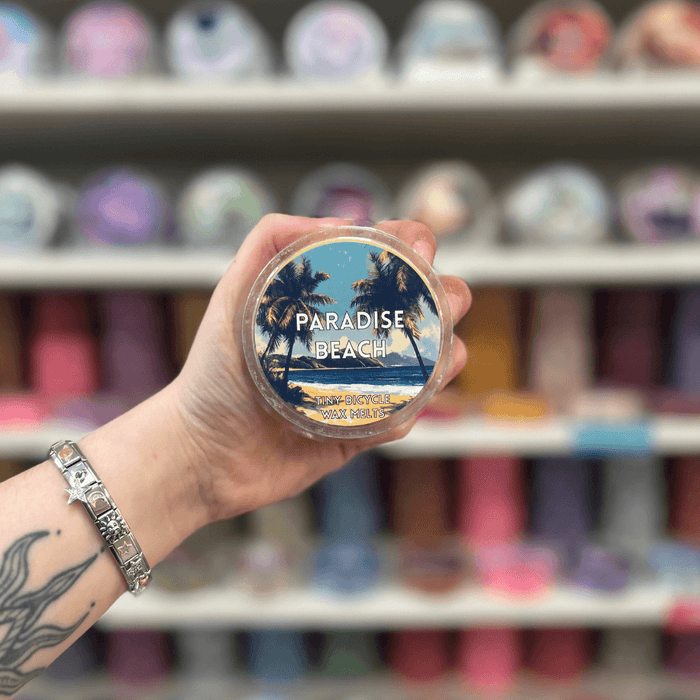 Paradise Beach wax melt pot held in hand with colourful wax melt display in the background