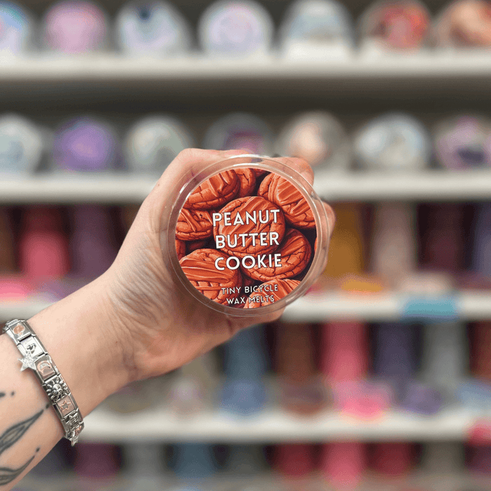 Peanut Butter Cookie wax melt pot held in hand with colourful wax melt display in the background