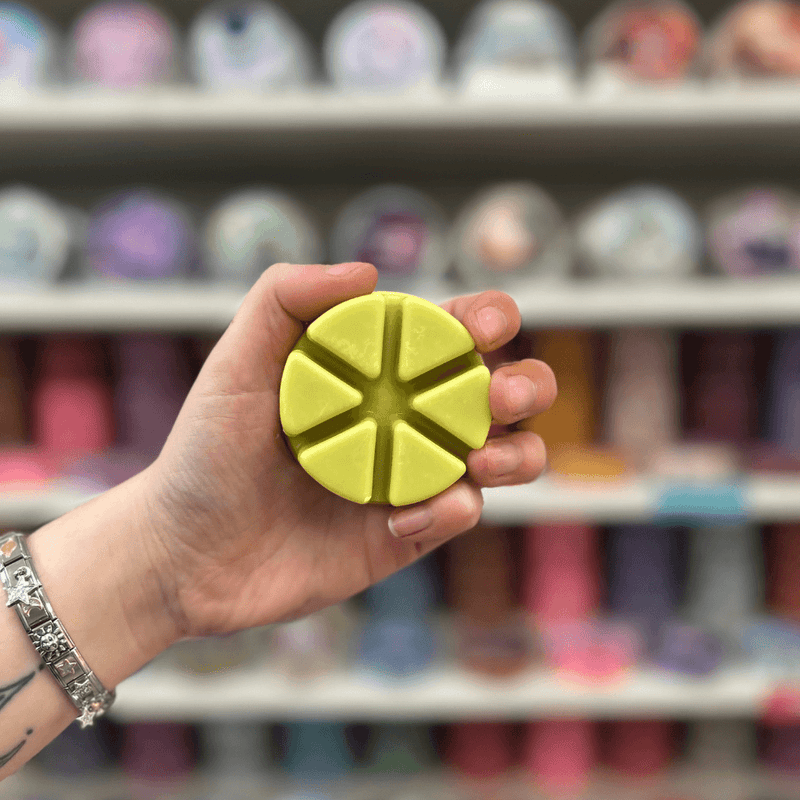 Pear and Freesia wax melt segments held in hand with colourful wax melt display in the background