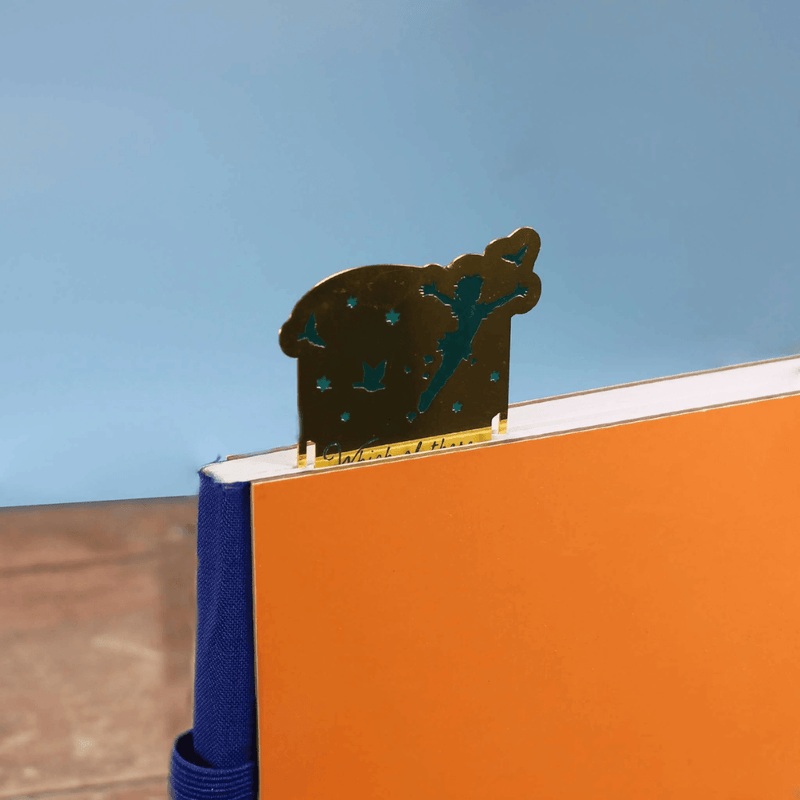 Peter Pan inspired gold metal bookmark peeking out from the top of a hardback book