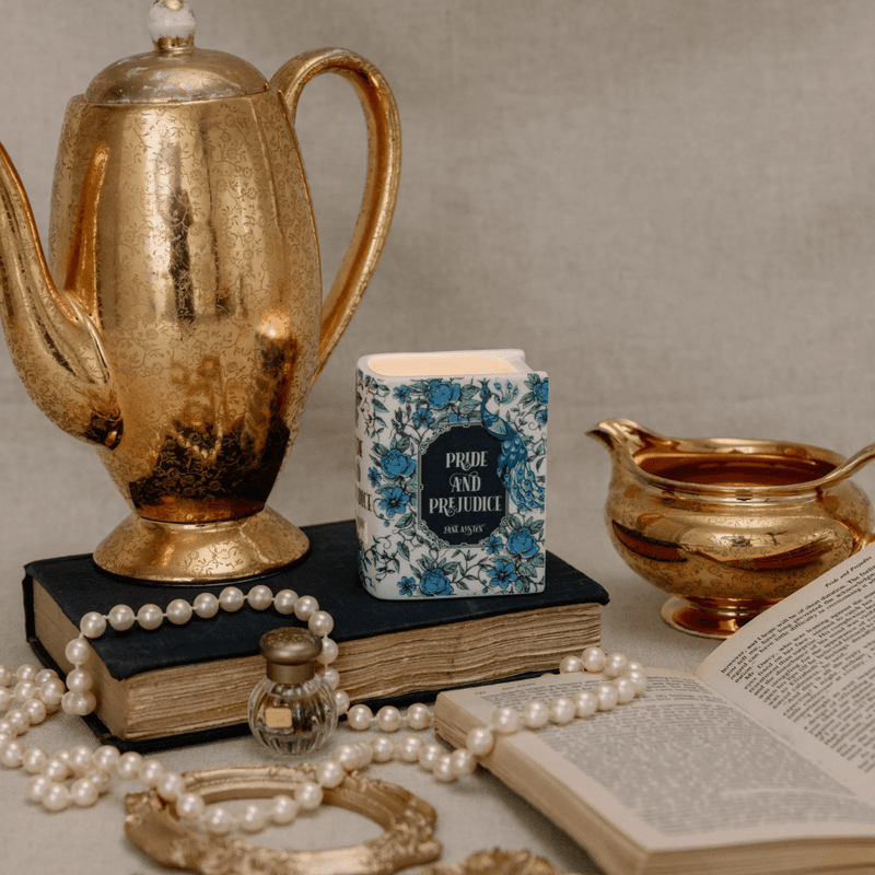 Pride and Prejudice book candle styled with a vintage teapot, pearls and an open book in a cosy scene.