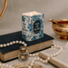Lit Pride and Prejudice book shaped candle on stacked books with pearls and a small perfume bottle.