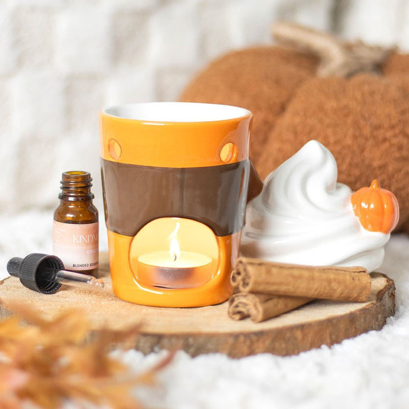Latte oil burner in use—tealight glowing inside while lid rests beside it on cosy backdrop.


