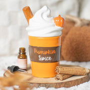 Pumpkin-spice latte–shaped ceramic oil burner styled on rustic wood slice with cinnamon sticks.
