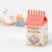 Random Cozy Cat milk-carton style blind box packaging on a white background with figures behind