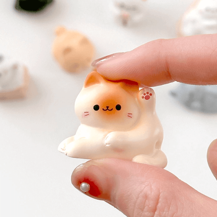 Miniature cosy cat figure held in hand showing the small size and pastel finish