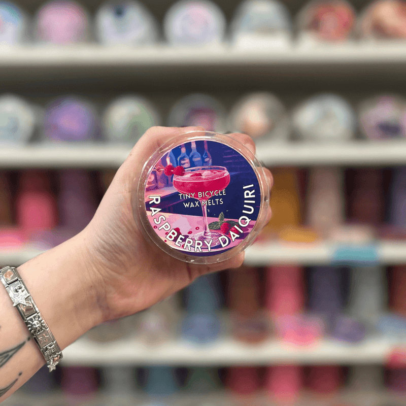 Raspberry Daiquiri wax melt pot held in hand with colourful wax melt display in the background