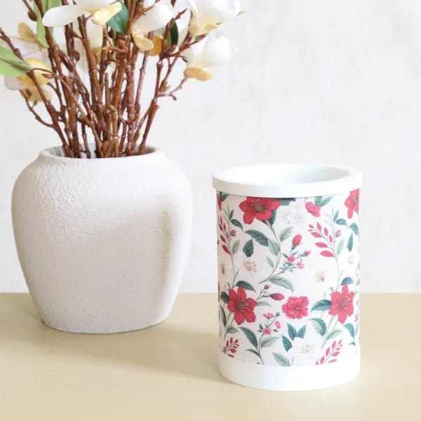 Red floral electric wax melt burner styled on a tabletop next to a neutral vase and stems.