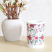 Red floral electric wax melt burner styled on a tabletop next to a neutral vase and stems.