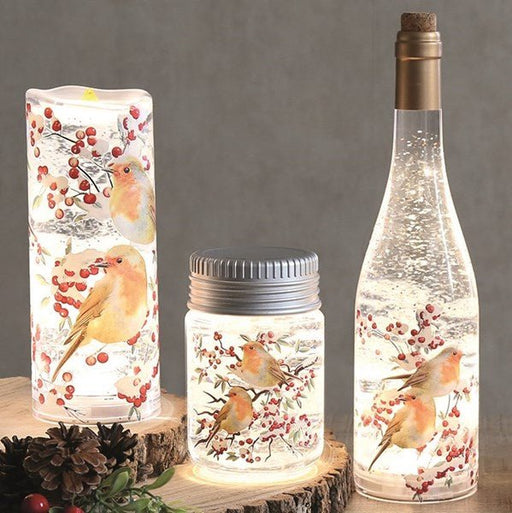 Lifestyle scene showing robin-themed LED water spinner jar glowing beside matching pieces on wooden slices.