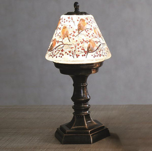 Lifestyle view of LED robin water spinner lamp glowing on a table, robins and berries shade.