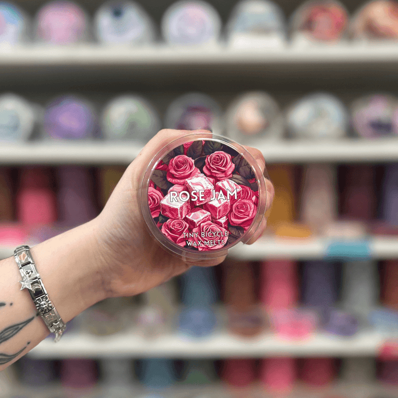 Rose Jam wax melt pot held in hand with colourful wax melt display in the background