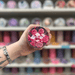 Rose Jam wax melt pot held in hand with colourful wax melt display in the background