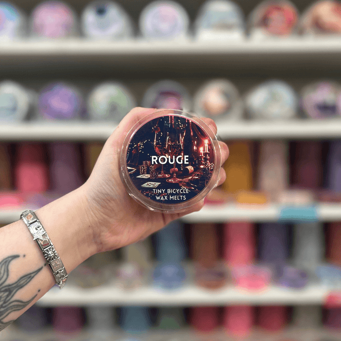 Rouge wax melt pot held in hand with colourful wax melt display in the background