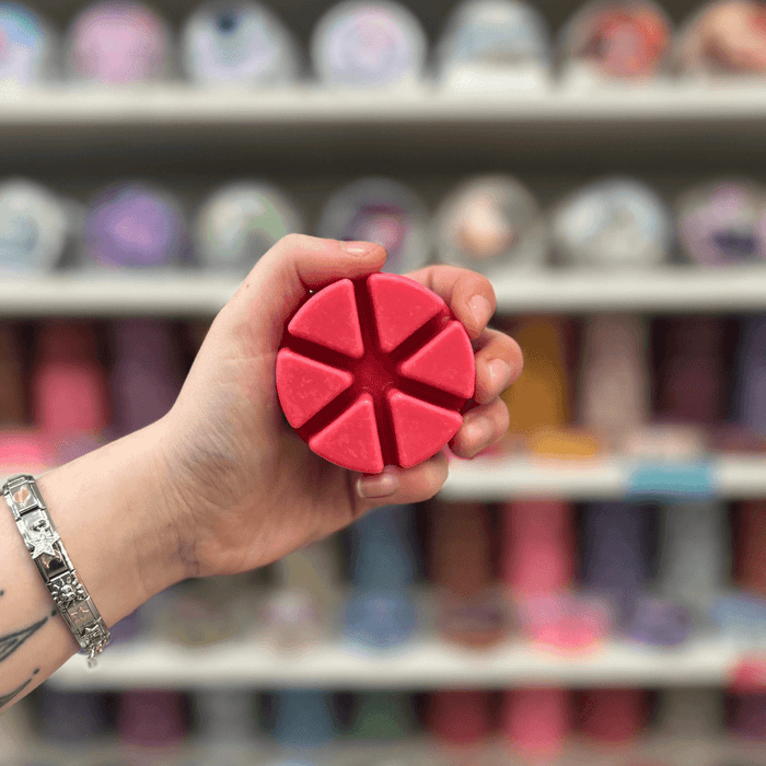 Rouge wax melt segments held in hand with colourful wax melt display in the background