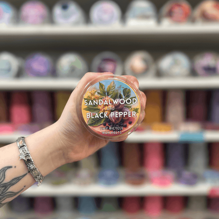 Sandalwood and Black Pepper wax melt pot held in hand with colourful wax melt display in the background