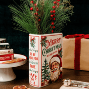 Santa Christmas book vase with winter greenery and red berries styled on a wooden table beside wrapped Christmas presents