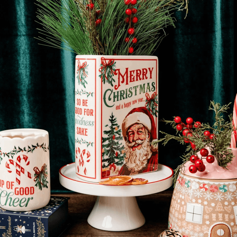 Santa ceramic book vase filled with festive greenery on a white stand, surrounded by coordinating Christmas home accessories