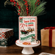 Reverse of Santa ceramic book vase filled with pine branches and red berries, styled with festive gift boxes