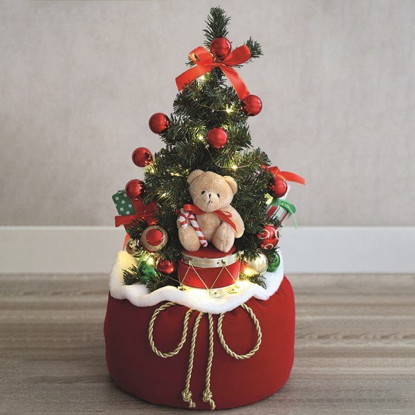 Lifestyle image of the 63cm LED tree glowing in a red Santa sack with presents and a toy drum.