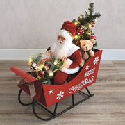 Lifestyle view of musical Santa in sleigh with presents and mini tree glowing on the floor.