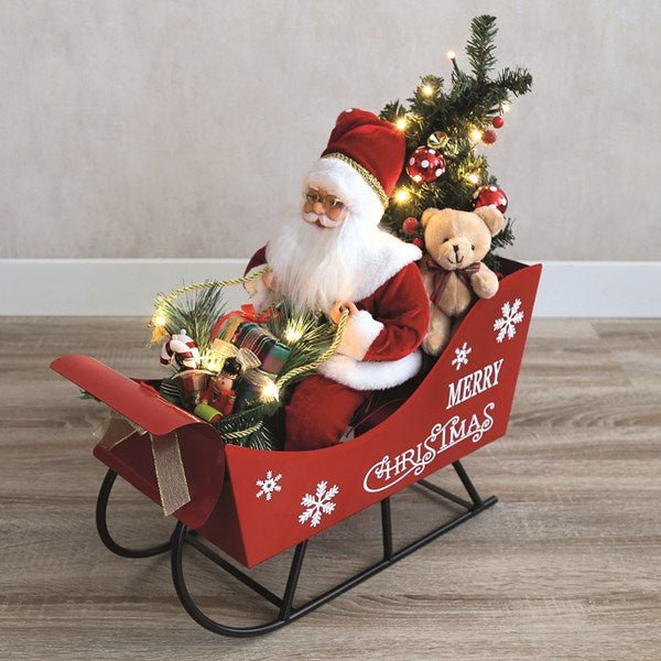 Lifestyle view of musical Santa in sleigh with presents and mini tree glowing on the floor.