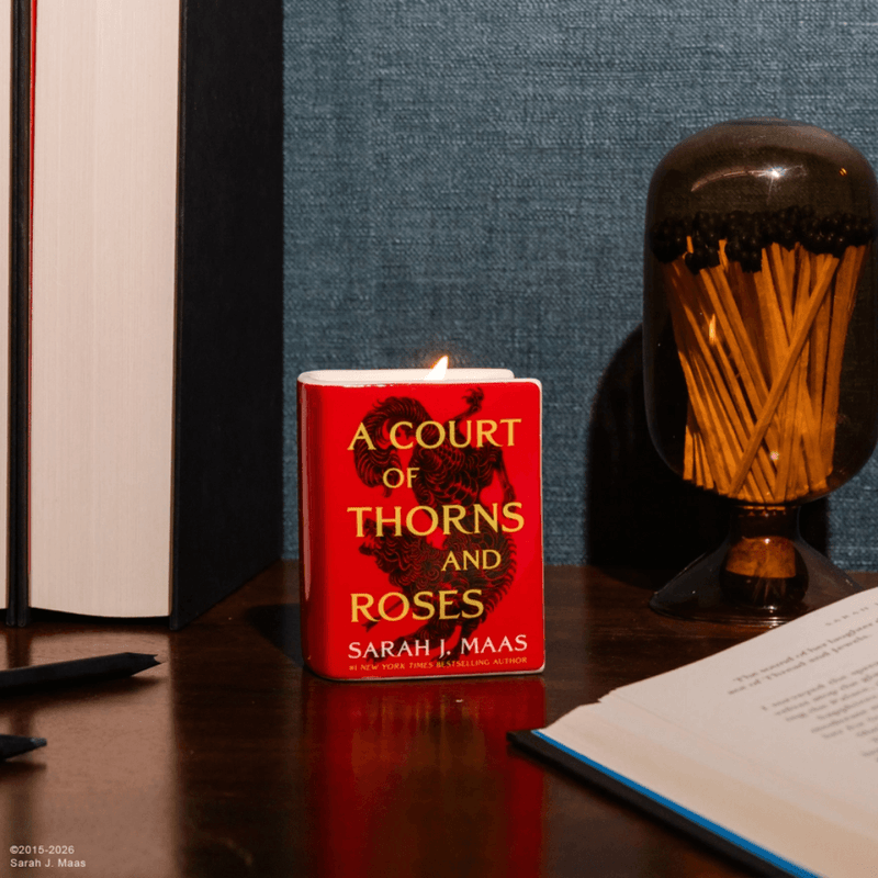 Lit ACOTAR book candle displayed on a desk beside books in a cosy reading nook