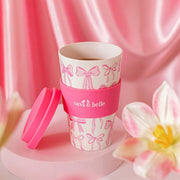Close-up of pink Sass & Belle bow travel coffee cup with lid on a pink background
