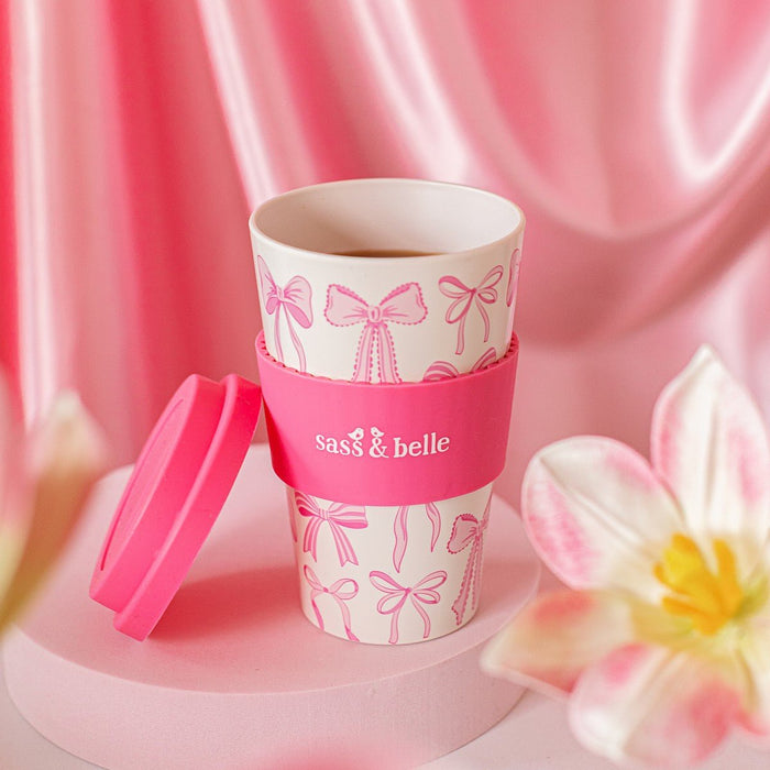 Close-up of pink Sass & Belle bow travel coffee cup with lid on a pink background