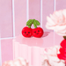 Sass and Belle cherry pocket token styled on a pink background with red cherries and green leaf detail