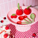 Cherry salt and pepper shakers styled on a pink cake stand with cherry kitchen accessories