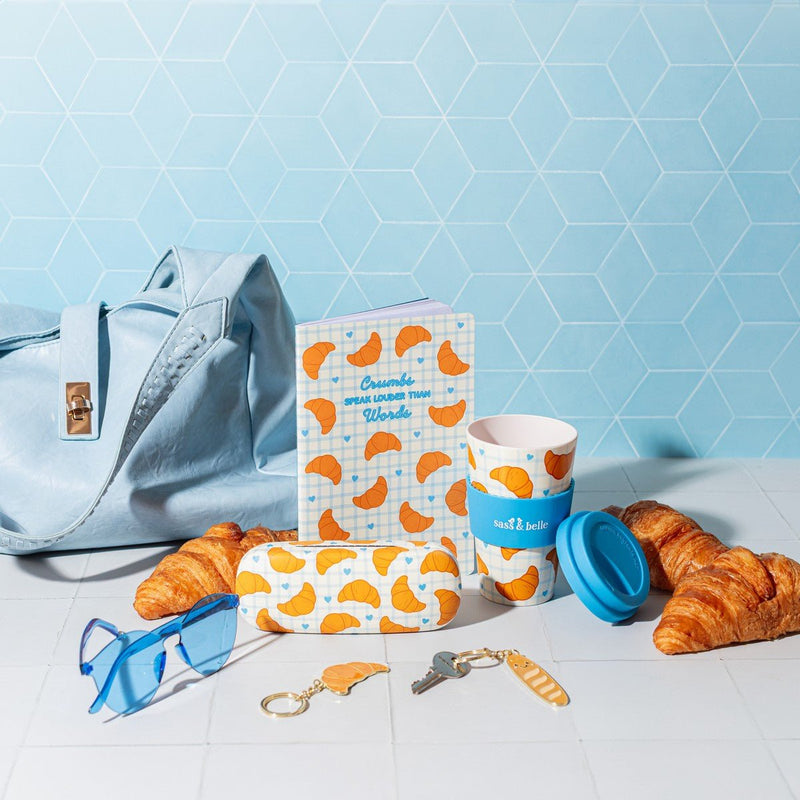 Sass & Belle croissant travel coffee cup with croissant notebook and accessories on a blue background