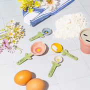 Sass & Belle flower measuring spoons displayed in a pastel kitchen with baking ingredients