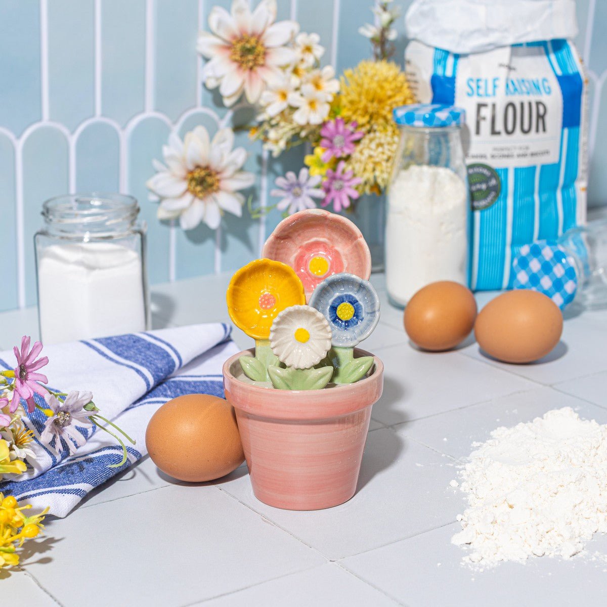 Sass & Belle flower measuring spoons with flour and eggs on a tiled kitchen counter