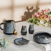 Lifestyle shot of Sass & Belle Mojave cat salt and pepper shakers with matching tableware and flowers on wooden surface

