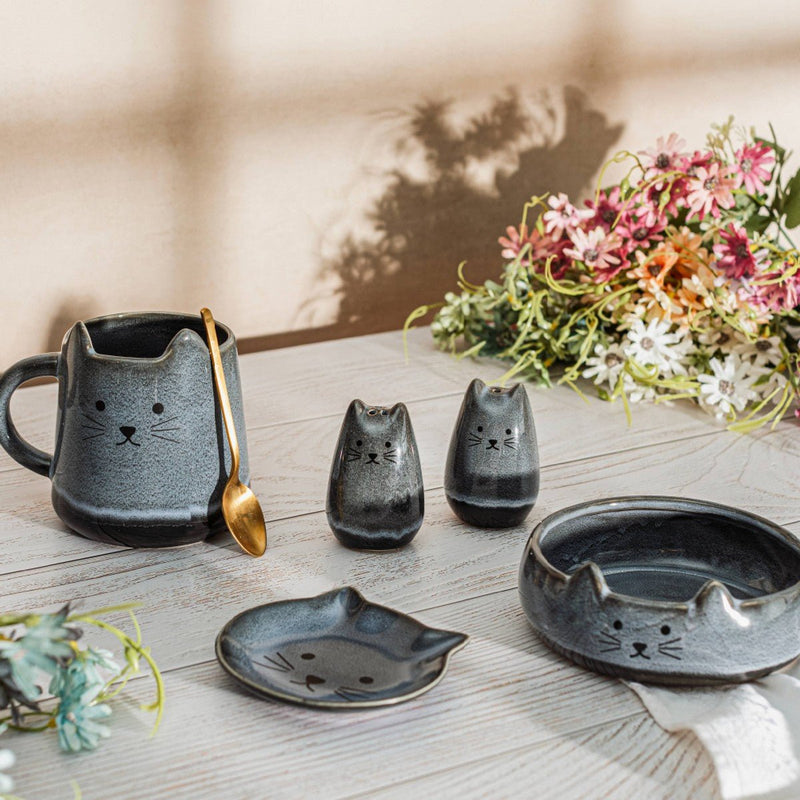 Lifestyle shot of Sass & Belle Mojave cat salt and pepper shakers with matching tableware and flowers on wooden surface

