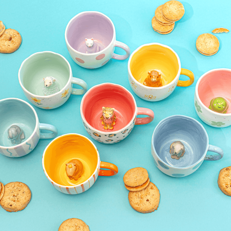 Sass and Belle surprise animal mugs styled with biscuits, showing colourful mugs with hidden animal designs inside