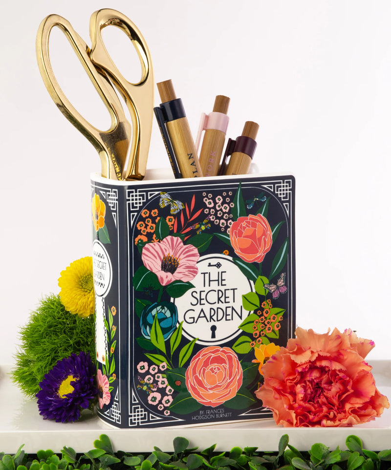 Secret Garden ceramic book vase holding pens and scissors on a desk.