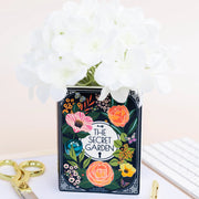 Secret Garden book-shaped vase filled with white flowers.
