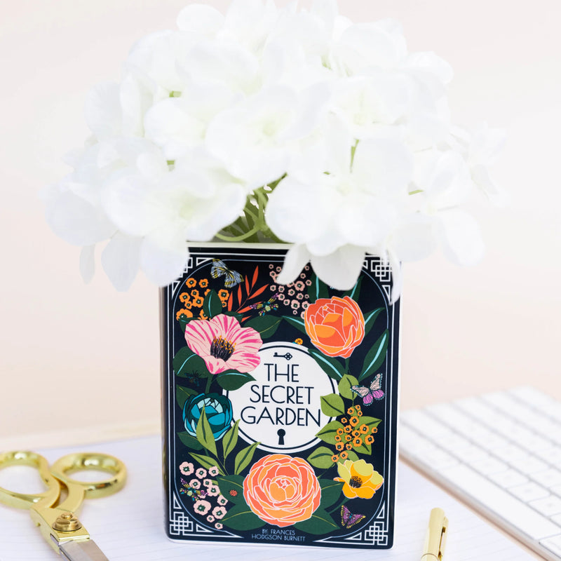 Secret Garden book-shaped vase filled with white flowers.