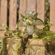 Signals green dragon plush by Charlie Bears Cuddle Cubs sitting on a mossy tree stump outdoors, small dragon soft toy